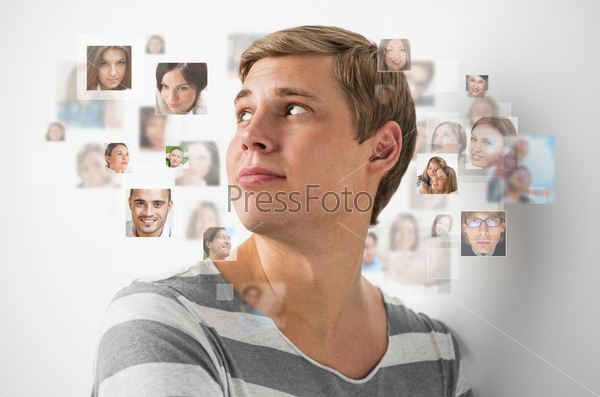 Young man standing and smiling with many different people\'s faces around him. Technology social media network of friends and communication.