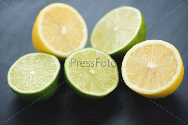 Fresh sliced limes and lemons, black wooden background