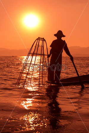 Silhouette of traditional fisherman in wooden boat using a coop-like trap with net to catch fish in Inle lake, Myanmar