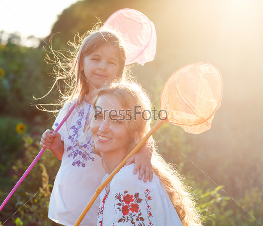 Cheerful mother and her daughter playing in a field with insect net in summer evening