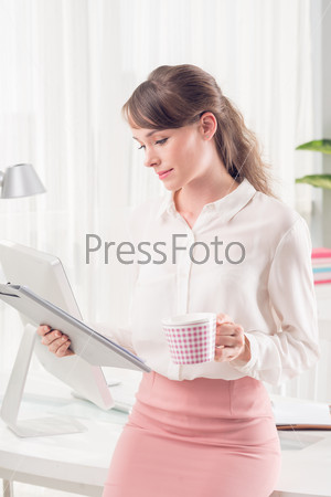 Vertical image of a young business lady working while having tea break at the office