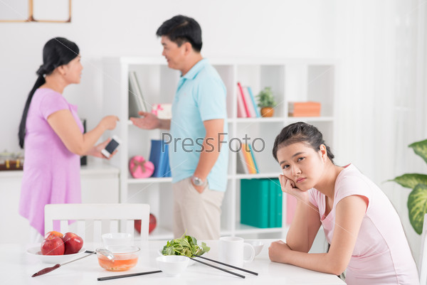 Close-up portrait of a tired teenage girl looking at camera while her parents quarreling on the foreground