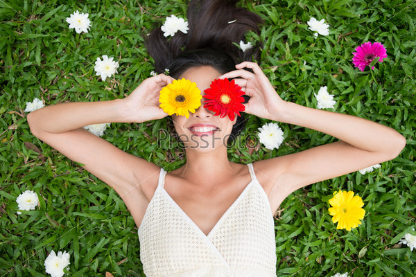 Angle view of a woman holding gerbera flowers on her eyes while lying on the grass