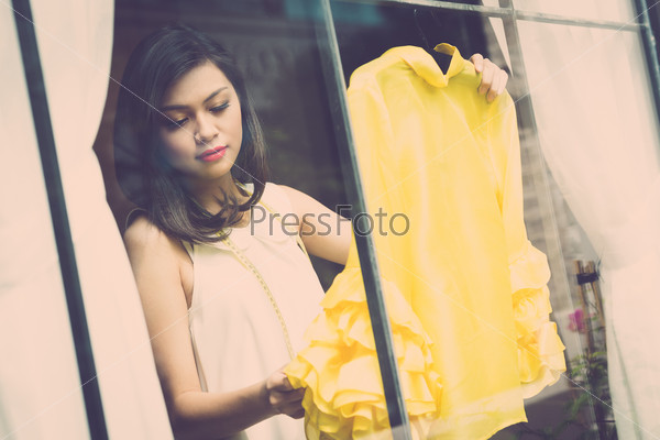 Close-up of a young shopwoman tailoring new clothes and photographing through the shop window