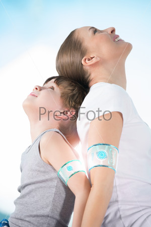 Mother and son wearing smart watch device sitting back to back together and looking upwards