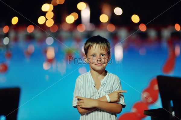 cheerful cute boy stands on a night the pool lights and reflection in water