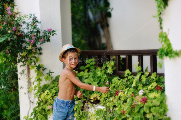 little boy in shorts and straw hat in a flower garden at home