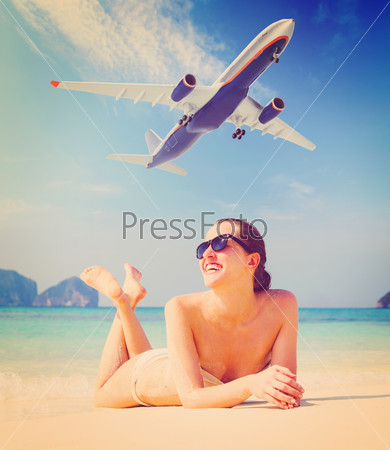 summer travel. young woman is lying on beach with aeroplane flying above