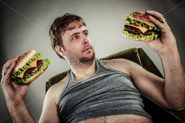 Fat man eating hamburger seated on armchair. Style fast food, stock photo