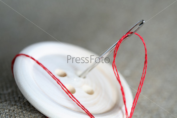Sewing concept. Closeup of wooden button and needle with red thread