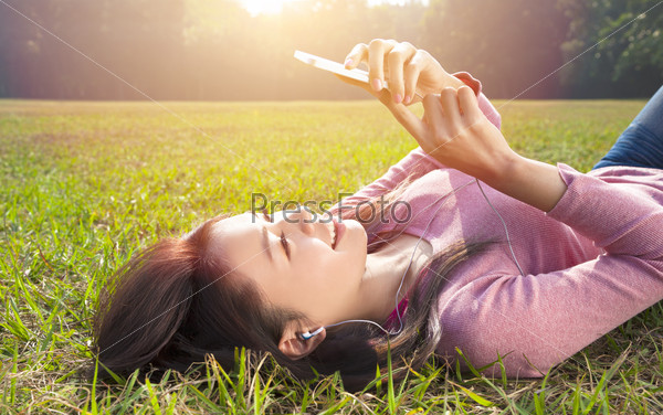 Smiling Young Woman Touching Cell Phone And Lying On Meadow
