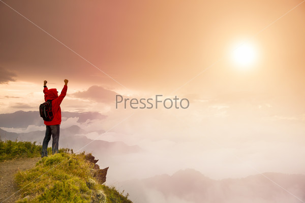 Young man with backpack standing  on top of  mountain watching the sunrise