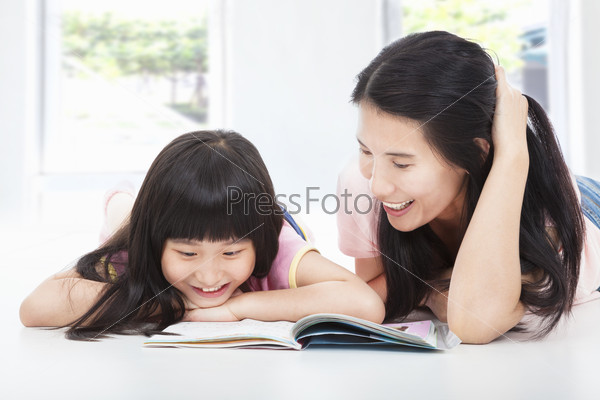 young  mother and her daughter lie on the floor and reading a book