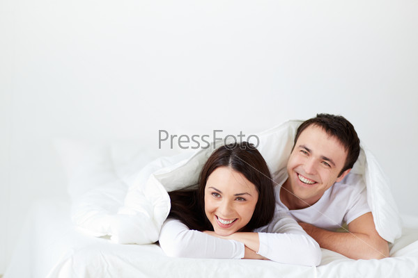 Portrait of joyful young couple lying in bed and laughing
