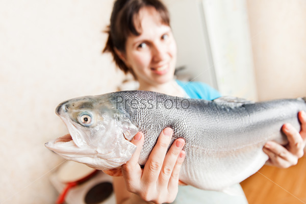 Healthy eating seafood - beauty young smiling woman hand holding raw salmon or trout fish food at kitchen