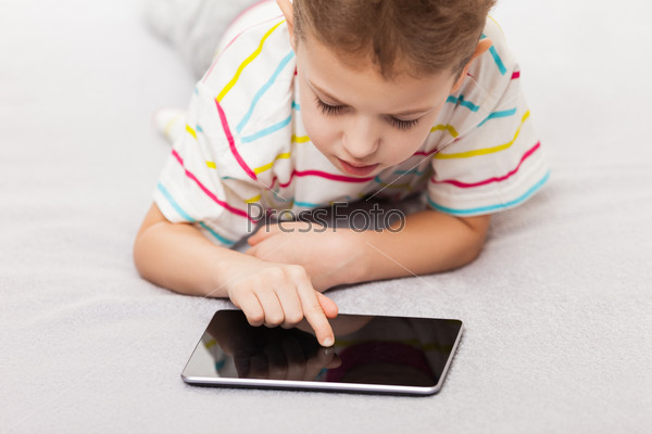 Little smiling child boy playing games or surfing internet on digital tablet computer