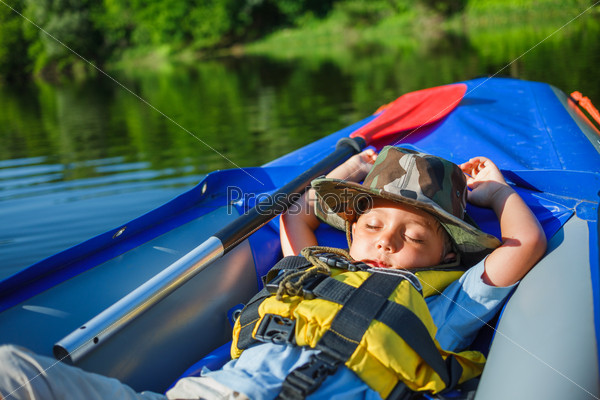Cute little boy sleeping in kayak on the river at a lovely summer day.