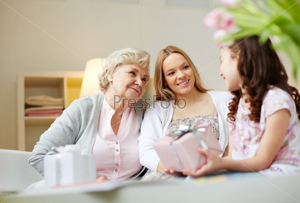 Portrait of happy little girl, her mother and grandmother with giftboxes talking at home, stock photo