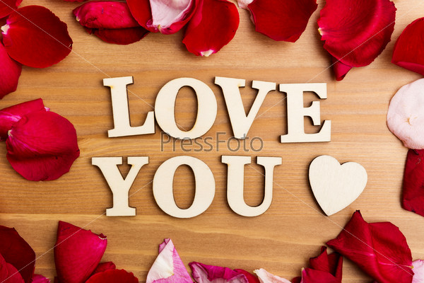 Wooden letters forming phrase Love You with rose petal besides