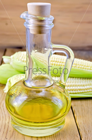 Corn oil in a glass carafe with corn cobs on the background of wooden boards