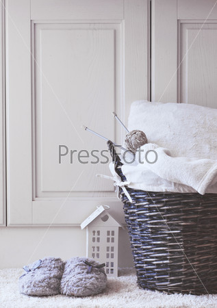 Wicker basket with warm blanket and knitting in it and soft slippers near it