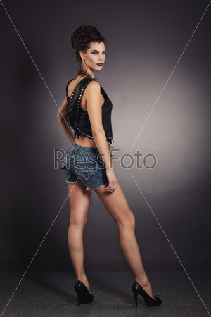 Sexy woman rocker image with creative make-up blue, black jacket and jeans shorts. Woman standing back and looking at the camera