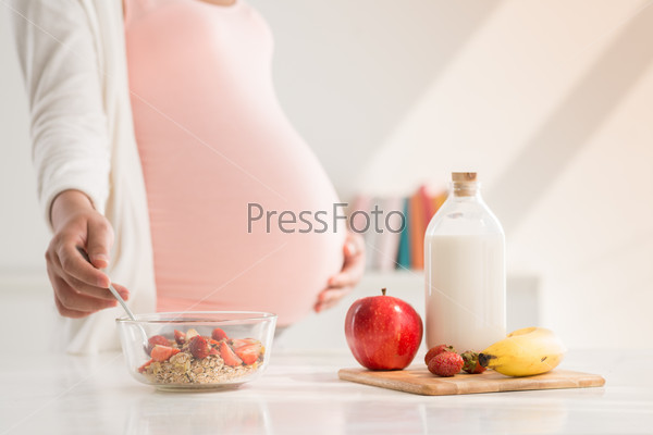 Pregnant woman preparing meal with milk and fruits