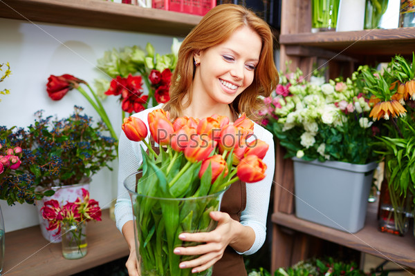 Portrait of young female florist with big vase of red tulips, stock photo