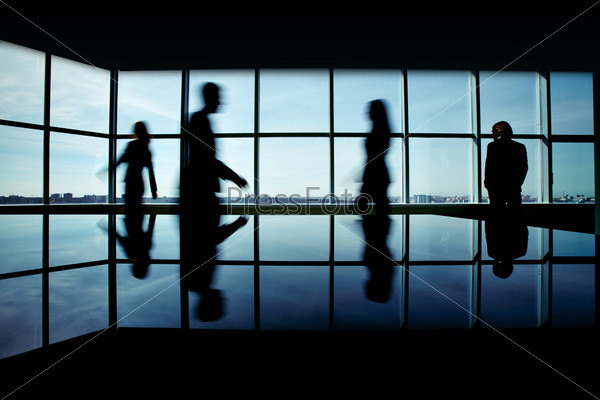 Silhouettes of several office workers on background of window