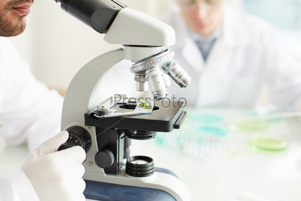 Male clinician studying bio sample in microscope, stock photo