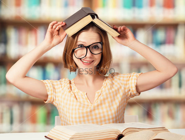 Tired funny crazy girl student with glasses reading books in the library, stock photo