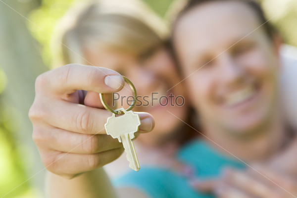 Happy Couple Holding Blank House Key Outside with Room For Your Own Text On The Key.