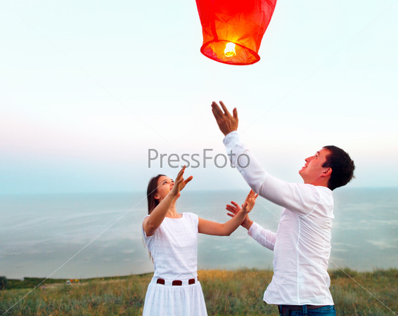 Young couple start a red Chinese sky lantern in the dusk near the sea