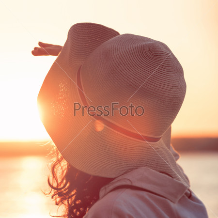 Young and beautiful woman wearing a hat in sunset light looking far away. Retro style photo from behind