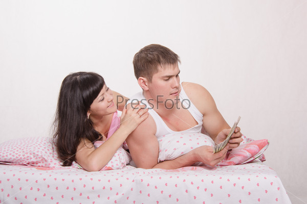 Young couple with money lying in bed, stock photo