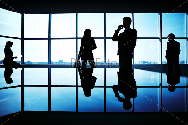 Silhouettes of several office workers working on background of window