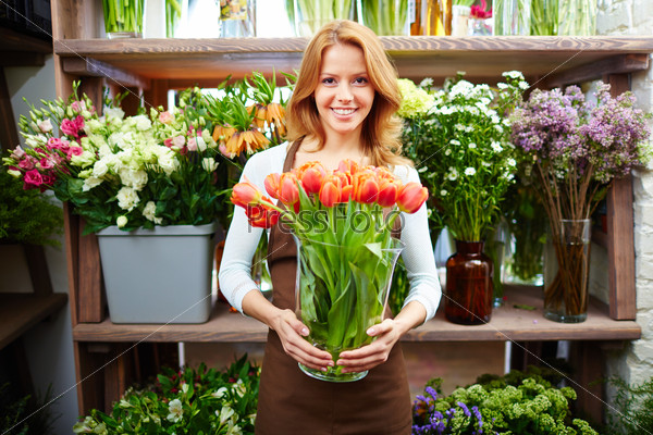 Portrait of happy female florist with big vase of red tulips looking at camera