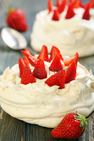 Pavlova dessert with strawberries and lemon cream on old wooden table.