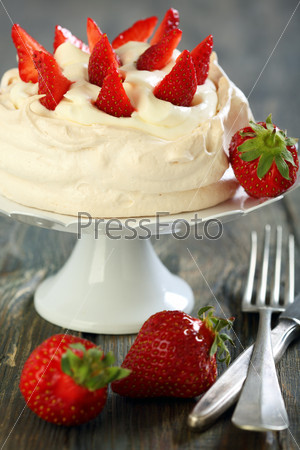 Meringue with whipped cream and strawberries on a white stand.