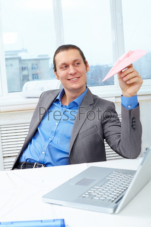 Happy businessman playing with paper plane in office