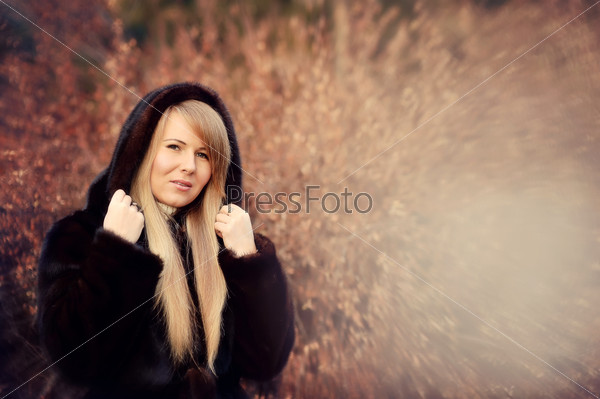 Outdoors portrait of a girl with long blond hair in a black fur coat
