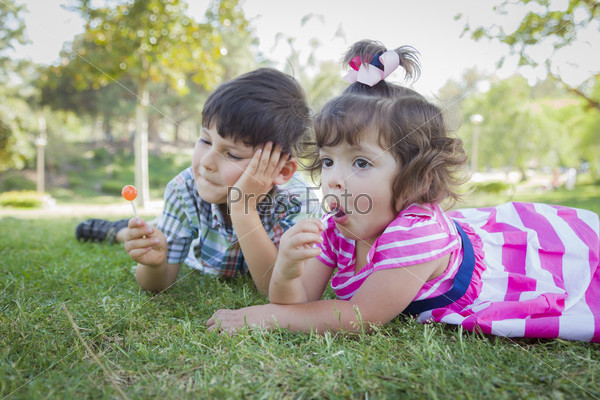 Cute Young Brother and Baby Sister Enjoying Their Lollipops Outdoors on the Grass.