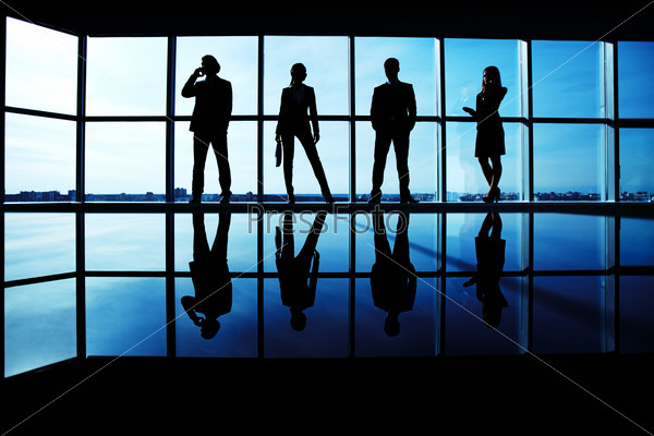 Silhouettes of several office workers standing by the window in line