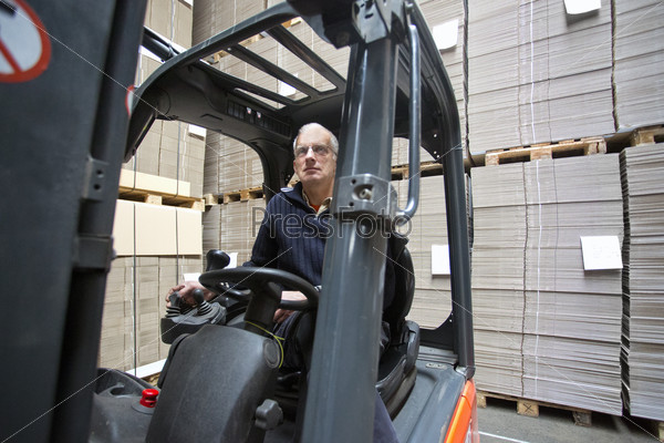 Forklift driver inside a forklift, manipulating a joystick in a warehouse full of pallets empty, plano, cardboard boxes