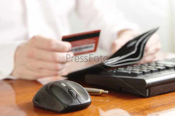 Hands of businessman with purse and bank card on the computer keyboard
