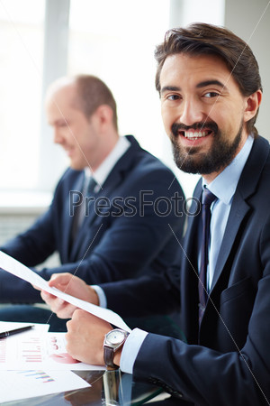 Image of young businessman working with papers on background of his colleague