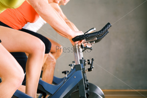 Three people working out on a stationary bicycle in the gym