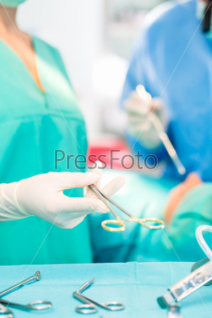 Hospital - surgery team in the operating room or Op of a clinic operating on a patient, perhaps it\'s an emergency a assistant holding a cotton swap forceps