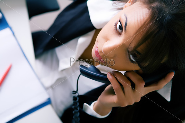 Latina in the office, phoning, looking at the viewer