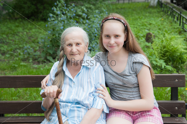 Granddaughter hugs grandmother sitting on a bench in the garden